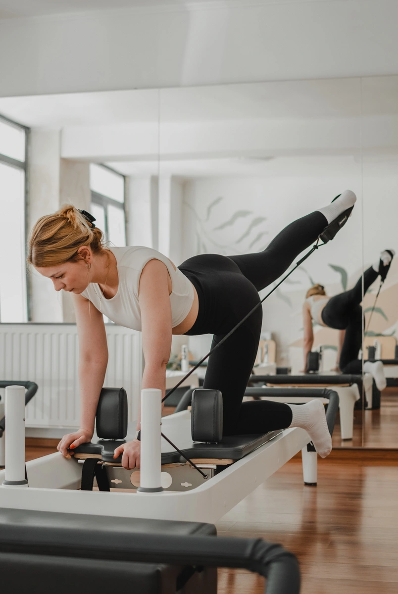 Nő reformer pilates gyakorlatot végez pilates gépen magasra emelt lábbal