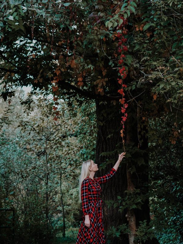 Portré őszi természetben fiatal, szőke, hosszú hajú nőről, piros kockás, hosszú ruhában piros leveleket érintve