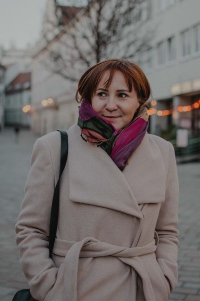 Városi portré fiatal nőről barna hajjal bézs kabátban